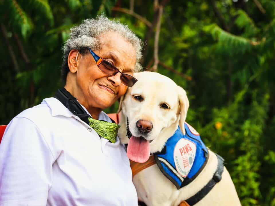 Vrouw met bril en begeleidingshond kijken blij in de camera